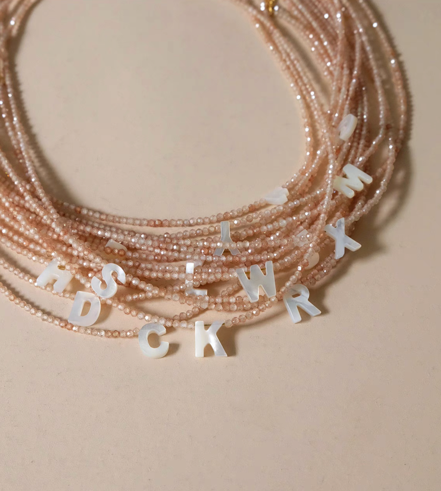Personalized shell initial necklace with multiple pearl letter charms on beaded chain showing natural stone detail close-up