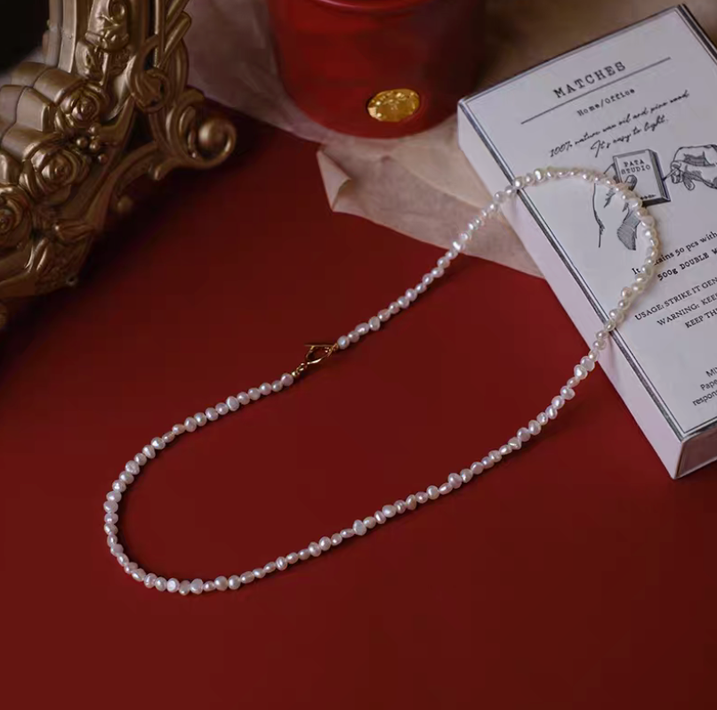 Petite baroque freshwater pearl necklace with 2.5 to 3mm pearls in natural color displayed on red background