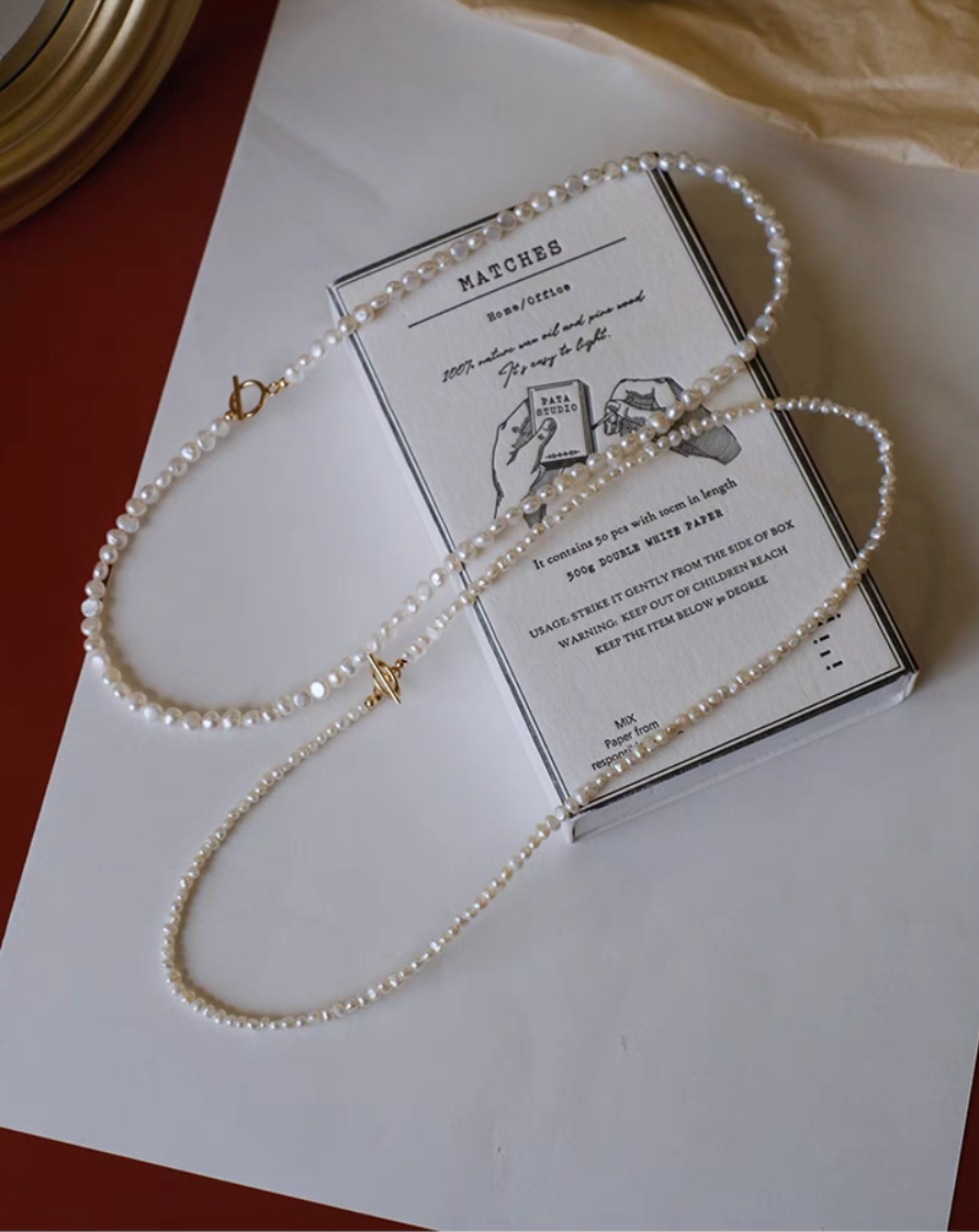 Petite 15 inch baroque freshwater pearl single strand necklace in natural color displayed with multiple pearl sizes on surface