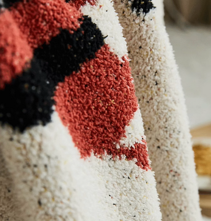 Macro texture of beige blanket highlighting red and black yarn fibers with soft plush looped surface