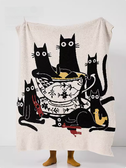 Beige throw blanket held open featuring multiple black cats gathered around illustrated teacup centerpiece