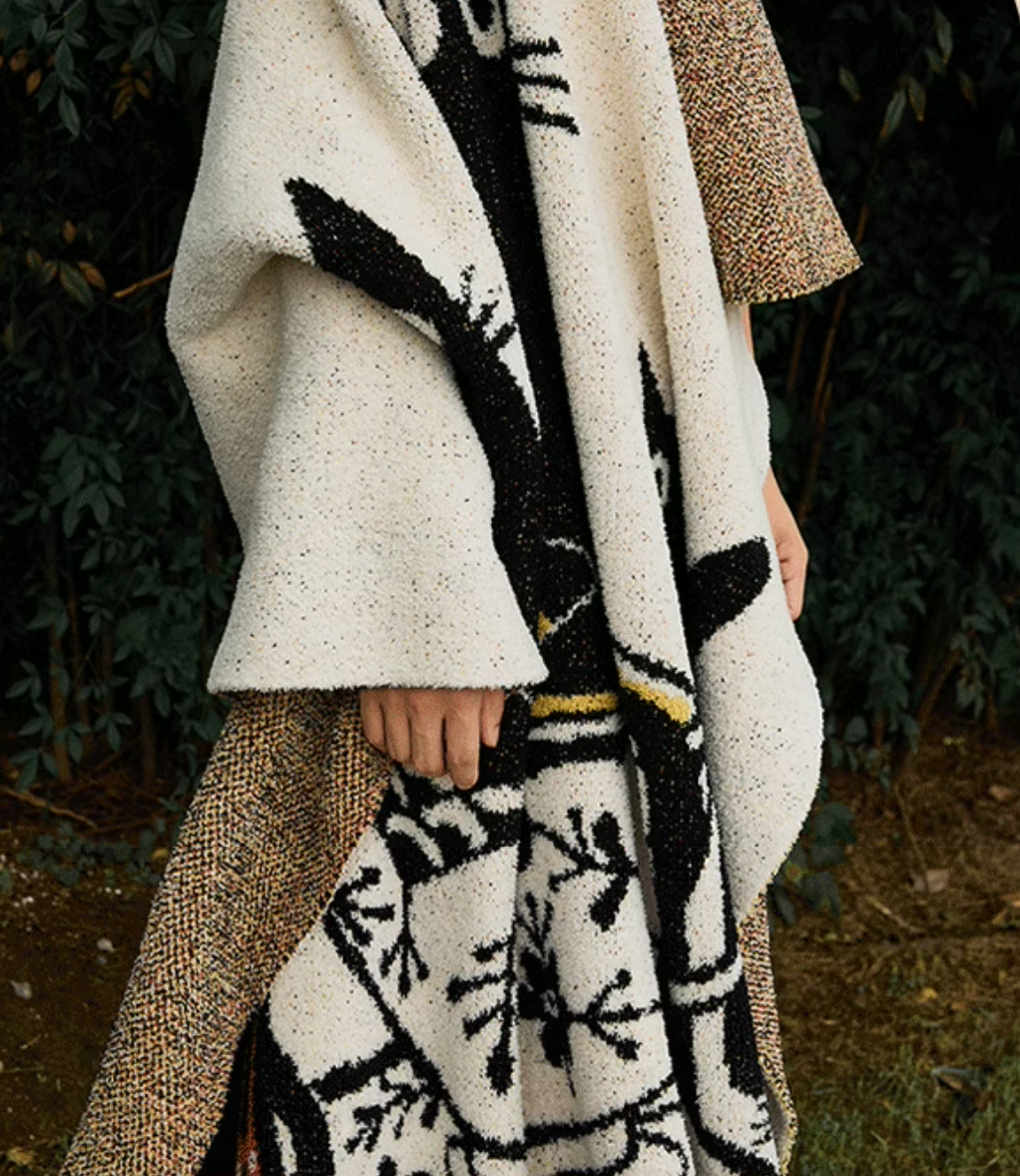 Person wearing beige cat tea party blanket outdoors showing flowing drape and large-scale cat illustration