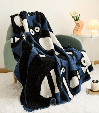 Blue and black cat blanket draped over chair in living room with lamp and flowers highlighting cozy styling