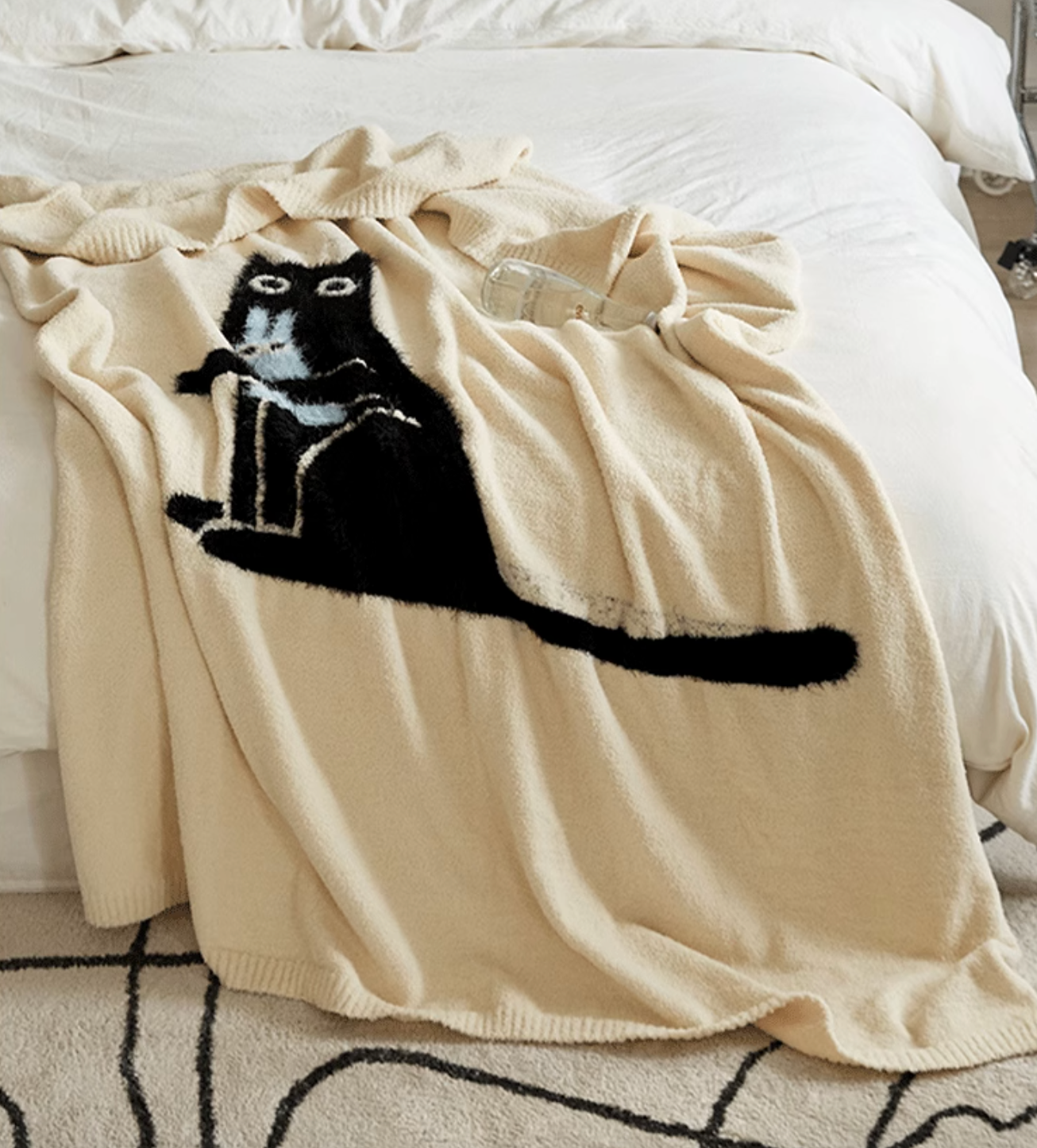 Ivory cat blanket spread across bed with long black cat silhouette extending horizontally across soft surface