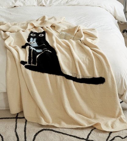 Ivory cat blanket spread across bed with long black cat silhouette extending horizontally across soft surface