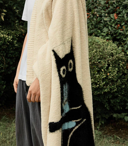 Close outdoor view of ivory blanket worn over shoulder showing elongated black cat graphic along fabric edge