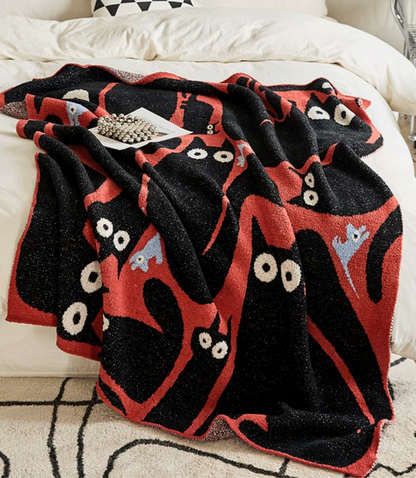 Red and black cat blanket layered on bed with visible folds emphasizing plush texture and scattered cat motifs