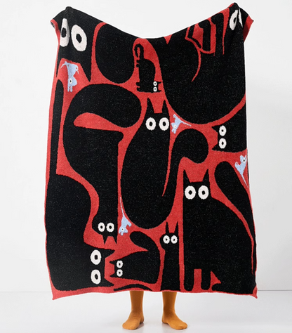 Red and black throw blanket held up fully featuring dynamic abstract cat shapes with small blue accents