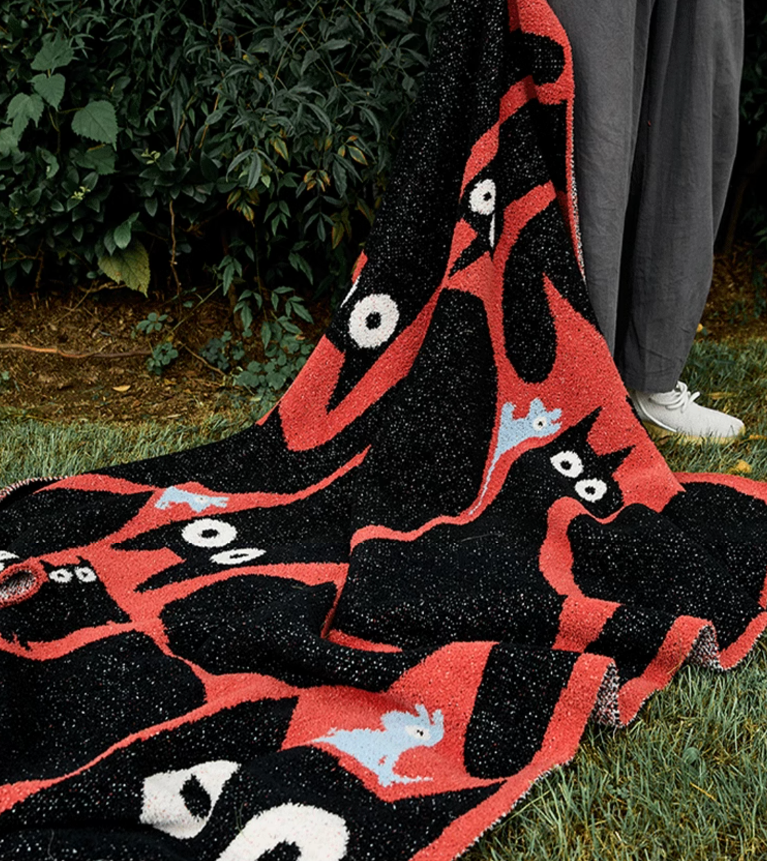 Red and black cat blanket spread across grass outdoors showing flowing fabric and bold high-contrast pattern