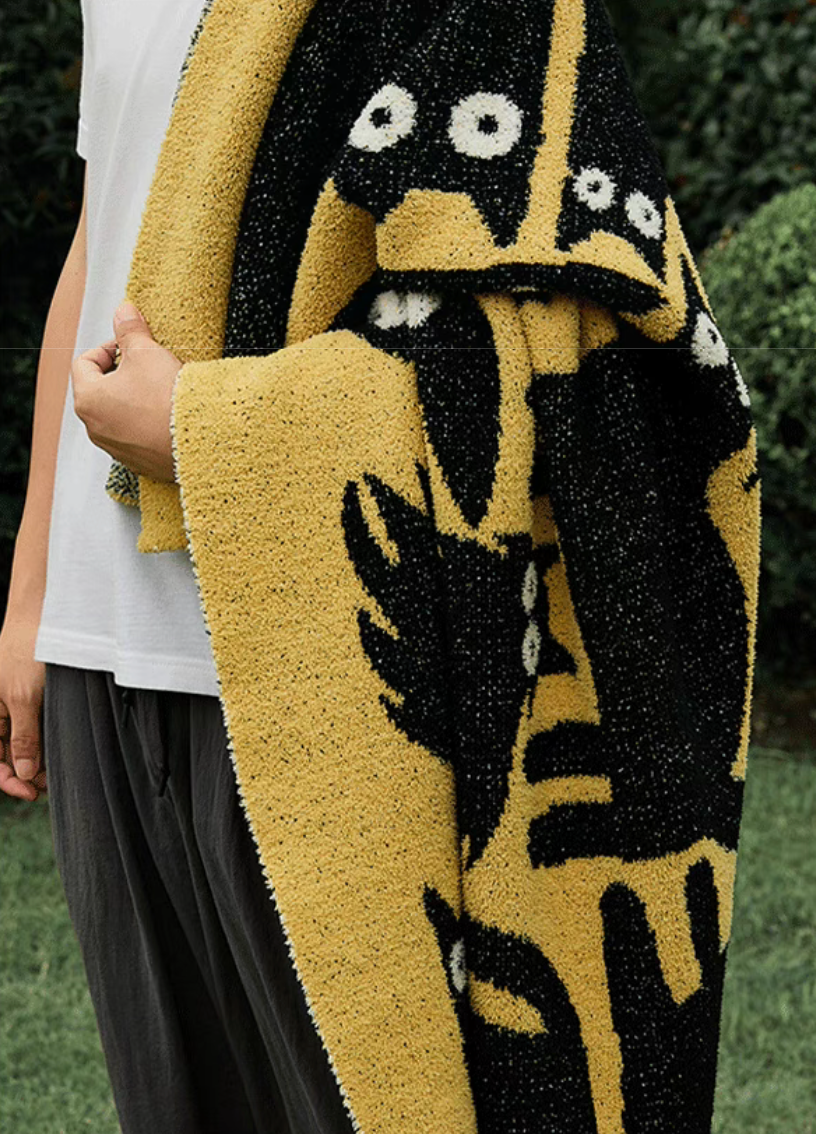 Close view of yellow cat blanket draped over arm showing fuzzy boucle texture and partial cat face details