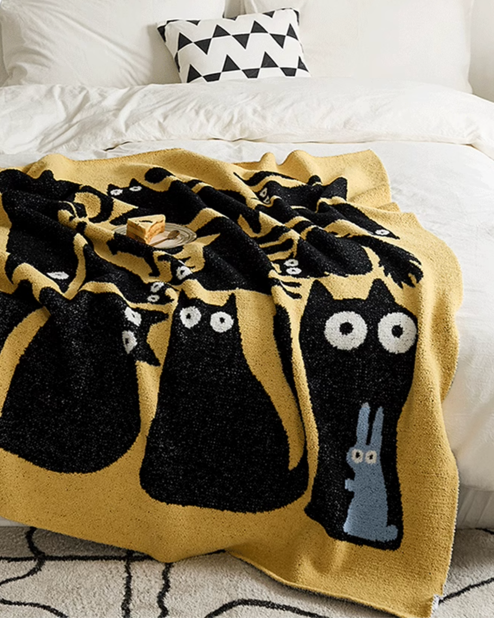 Yellow cat blanket spread across bed with tray on top highlighting playful black cat shapes and cozy bedroom setting