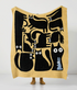 Yellow throw blanket held up fully displaying black abstract cats and a small blue figure with bold graphic layout