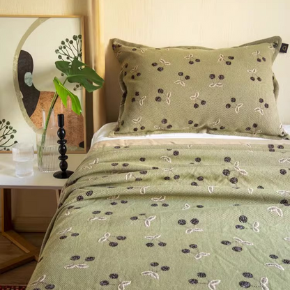 Playful Pals Cotton Gauze Quilted Blanket Black Cherry styled on a bed with green bedding and cherry pattern design