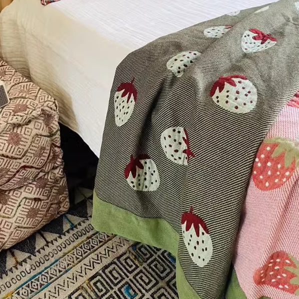 Playful Pals Cotton Gauze Quilted Blanket Strawberry reverse side in green with white strawberry pattern draped over bed edge