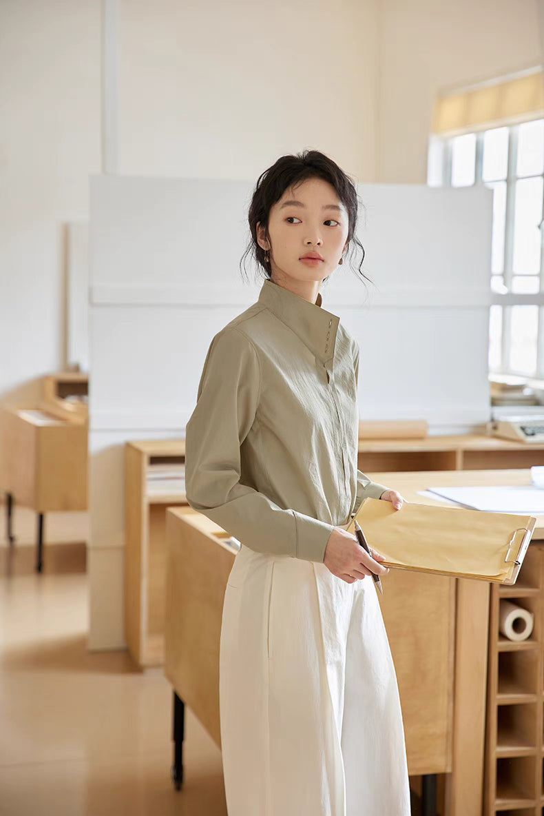 Model wearing Pleated Placket Stand-Collar Shirt in Teal standing in office setting holding folder, highlighting clean professional style and soft fabric