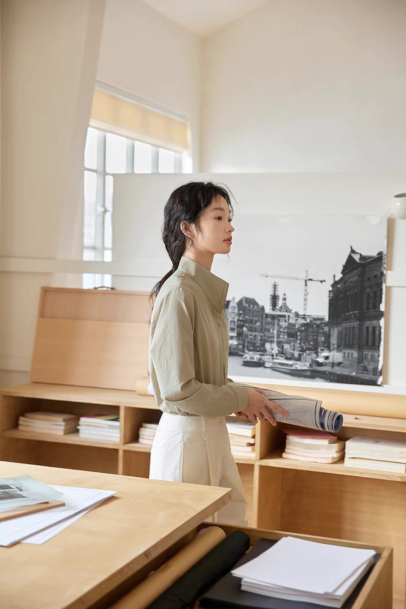 Side view of model wearing Teal Pleated Placket Stand-Collar Shirt walking in office space, showcasing relaxed silhouette and minimal design