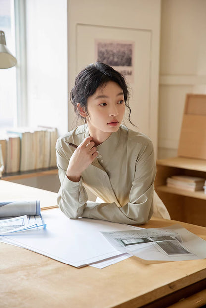 Teal stand-collar shirt styled in a work setting with model sitting at desk, emphasizing comfortable fit, pleated placket detail, and everyday office wear