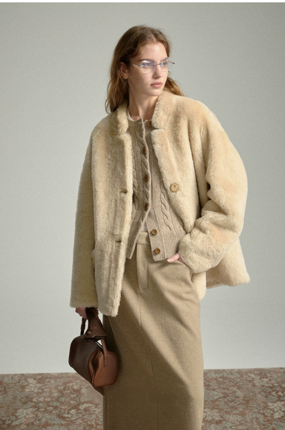Oat sheepskin shearling jacket worn over a cable-knit cardigan with a long knit skirt