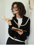 Model wearing black Poised Polo Knit Top with polo collar and button front, holding vintage telephone and notebook, front view