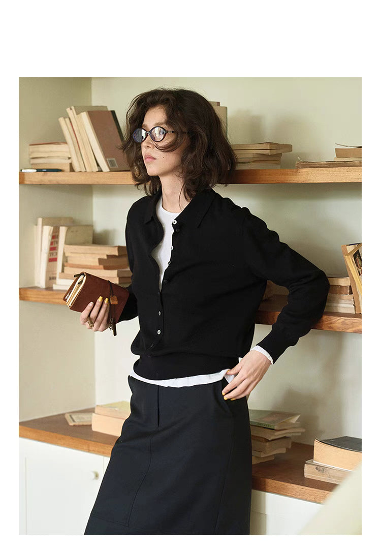 Model wearing black Poised Polo Knit Top paired with skirt, leaning against bookshelf, full body front view
