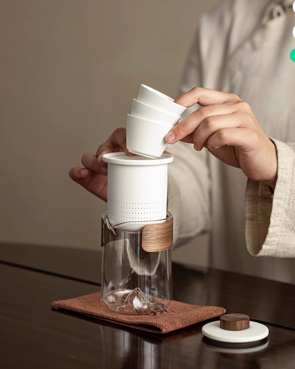 White portable outdoor travel tea set stacking ceramic cups onto infuser inside glass teapot