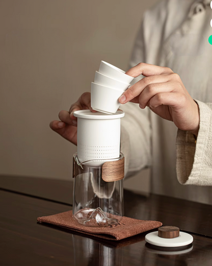 White portable outdoor travel tea set stacking ceramic cups onto infuser inside glass teapot