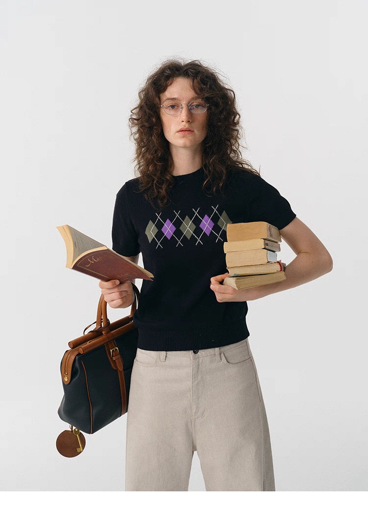 Model holding books while wearing black preppy argyle knit tee.