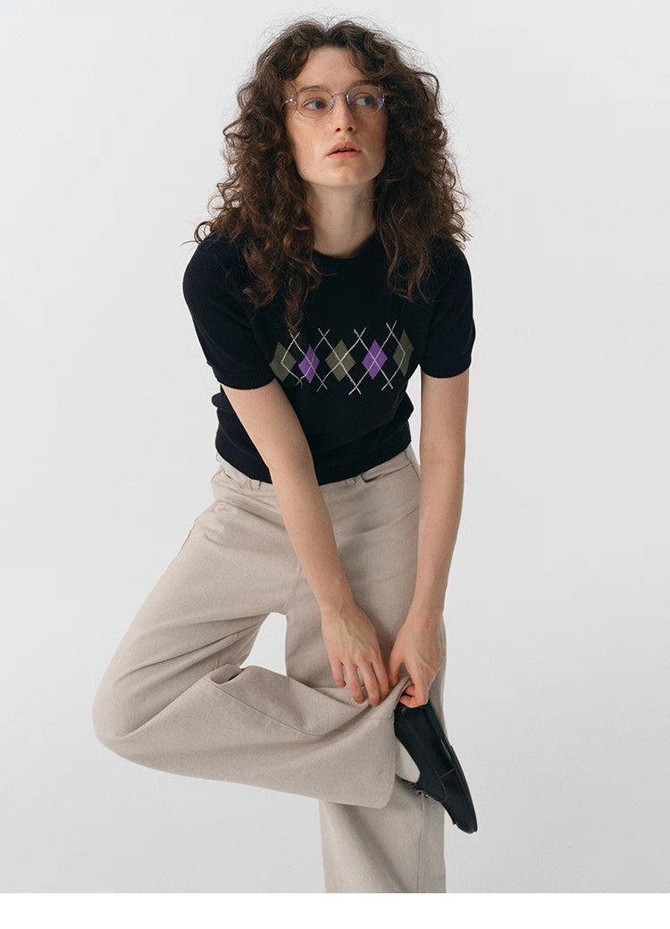 Full-body shot of model adjusting shoe while wearing black argyle knit tee.