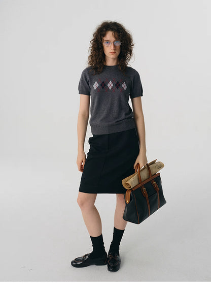 Full-body shot of model in charcoal argyle knit tee styled with black skirt and bag.