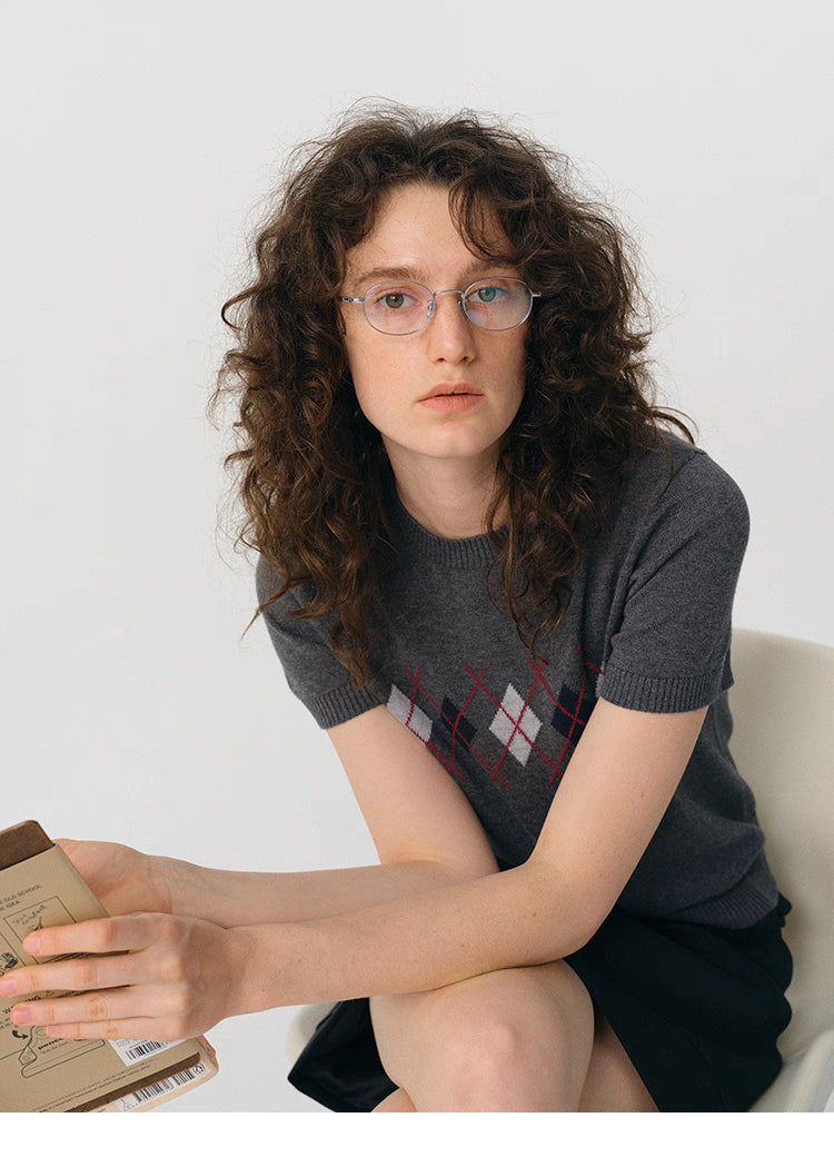 Model sitting with notebook while wearing charcoal argyle knit tee.