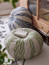 Green and blue pumpkin round floor cushions placed on the floor with an open book, styled in a cozy living room setting