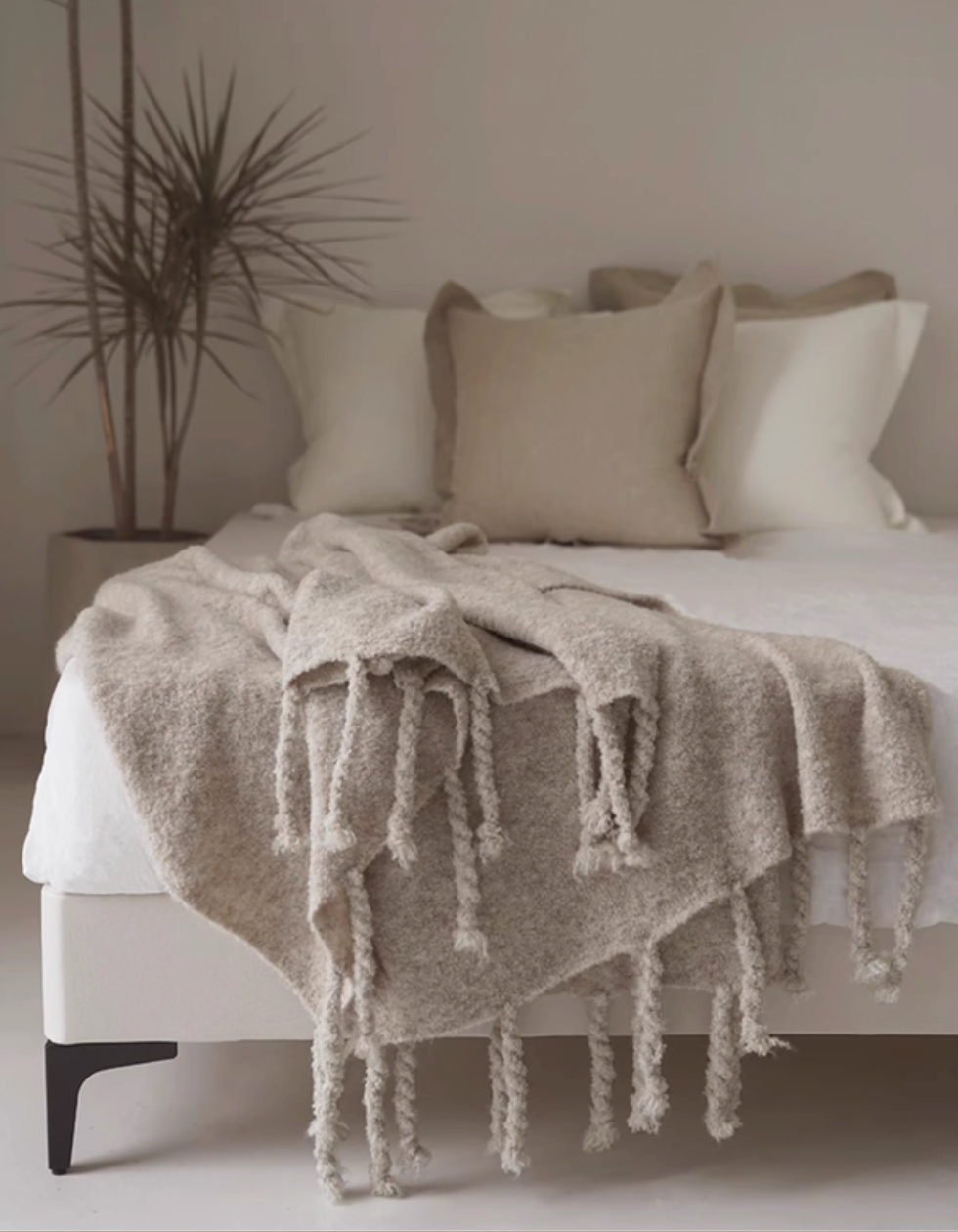Gray pure wool throw blanket styled across a bed with tassel fringe and layered neutral pillows