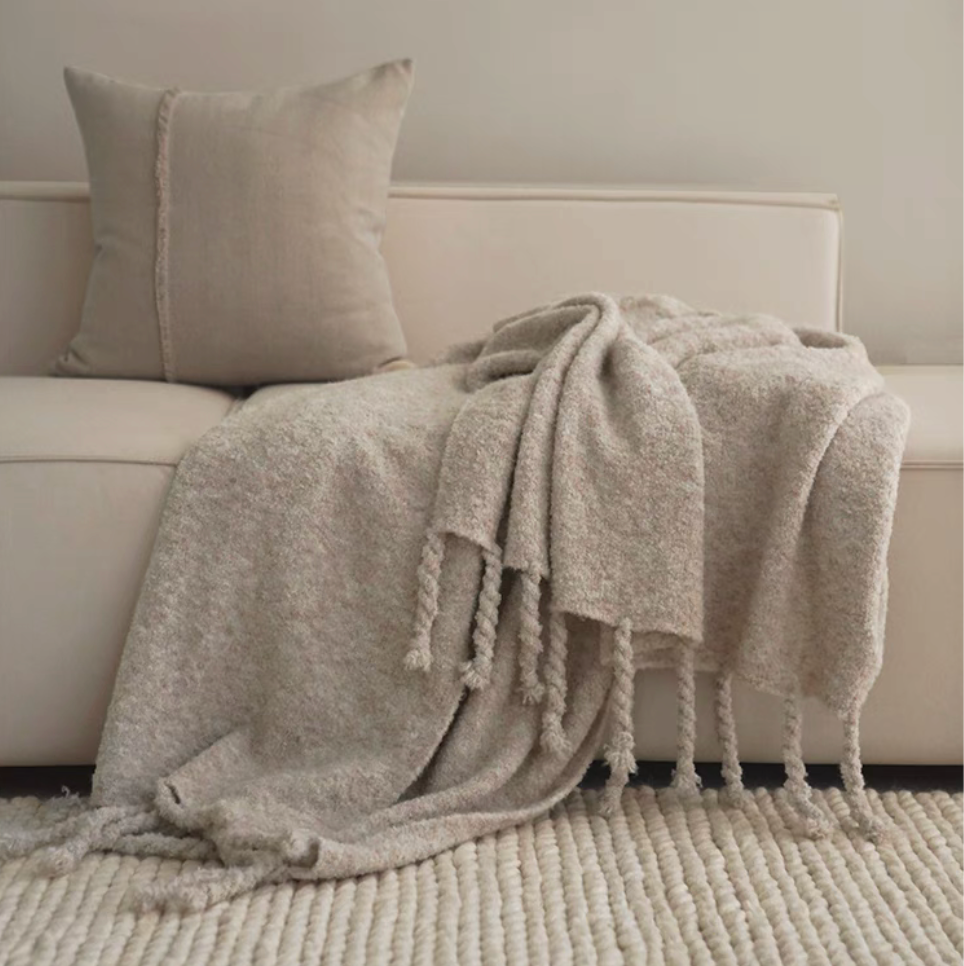 Gray pure wool throw blanket draped over a beige sofa with knotted fringe in a soft neutral living room