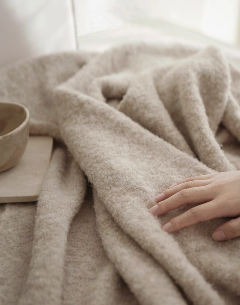 Close-up of gray pure wool throw blanket with soft plush texture and hand touching the fabric