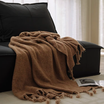 Mocha brown pure wool throw blanket draped over a black chair with soft folds and fringe tassels