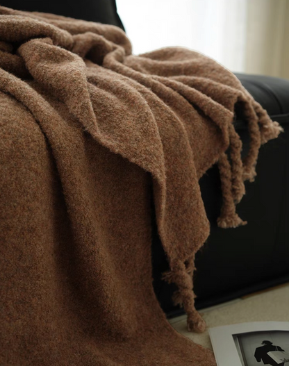 Mocha brown pure wool throw blanket hanging over a black chair with visible fringe and cozy texture