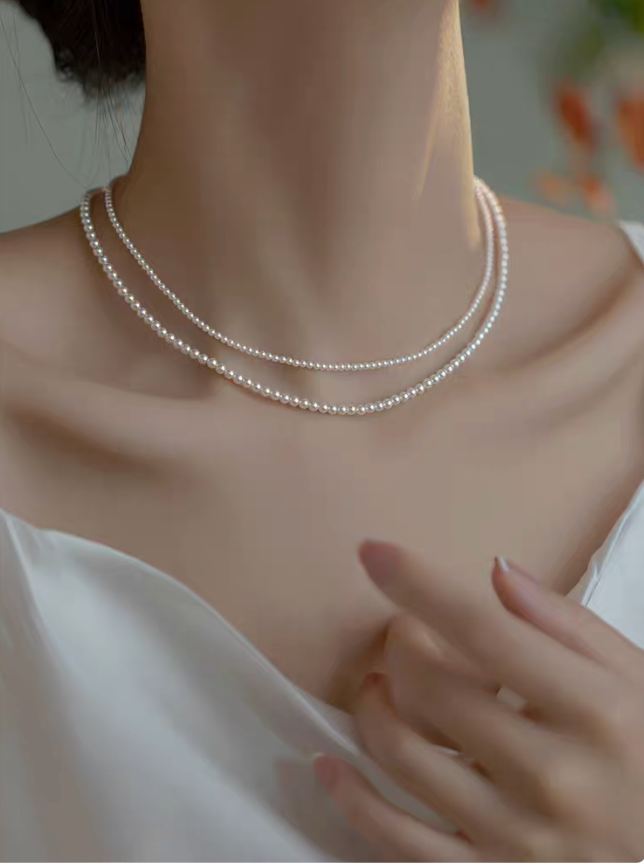 Model wearing layered Radiant Round Pearl Necklace in natural color with two round pearl sizes