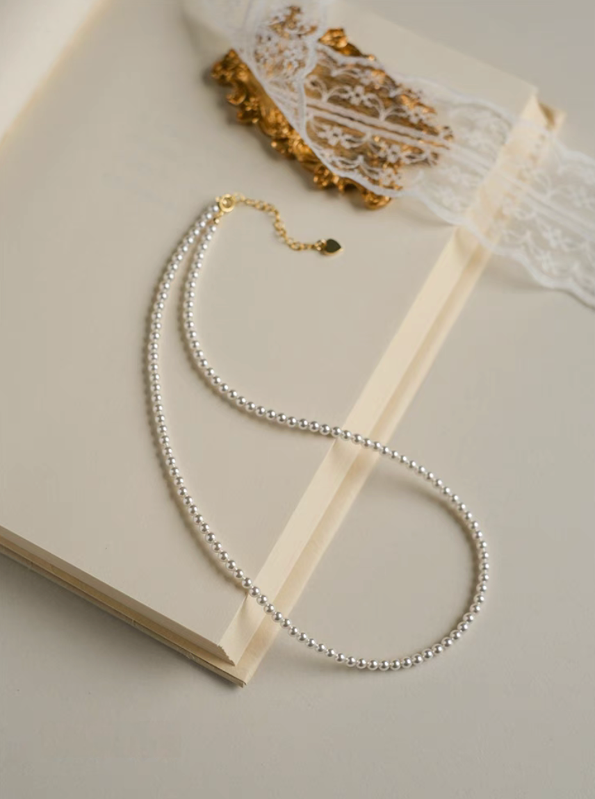 Radiant Round Pearl Necklace in natural color displayed as single strand on open book with lace detail
