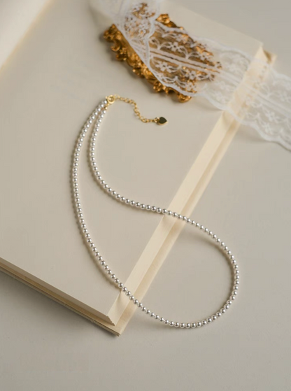 Radiant Round Pearl Necklace in natural color displayed as single strand on open book with lace detail