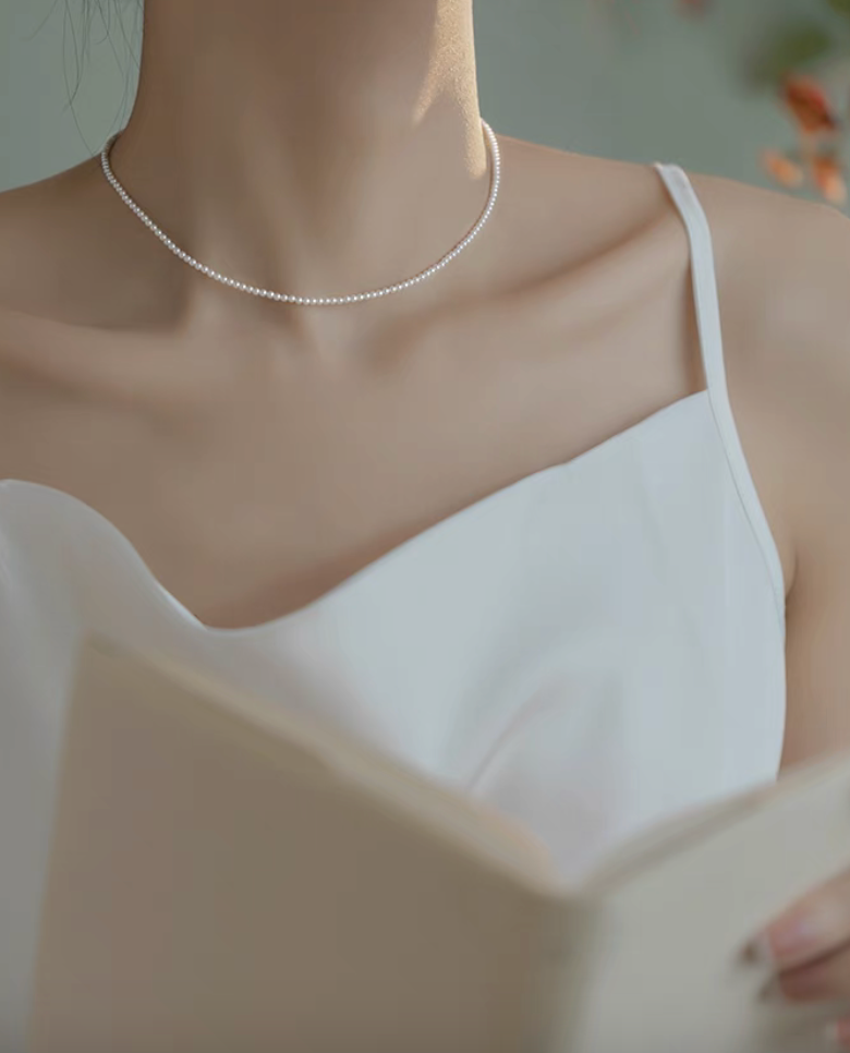 Model wearing Radiant Round Pearl Necklace in natural color while holding a book