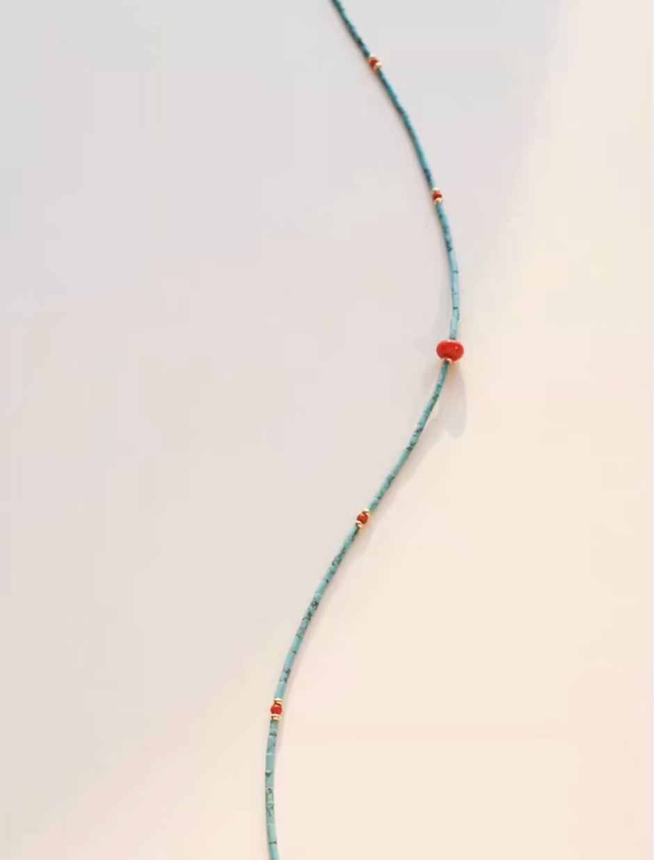 Close-up of turquoise seed bead strand necklace highlighting red agate drop pendant and gold accent bead details