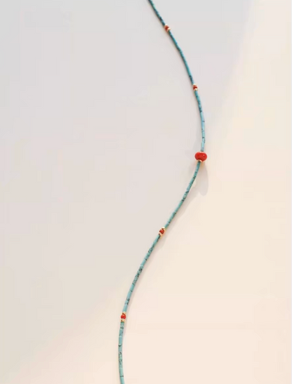 Close-up of turquoise seed bead strand necklace highlighting red agate drop pendant and gold accent bead details