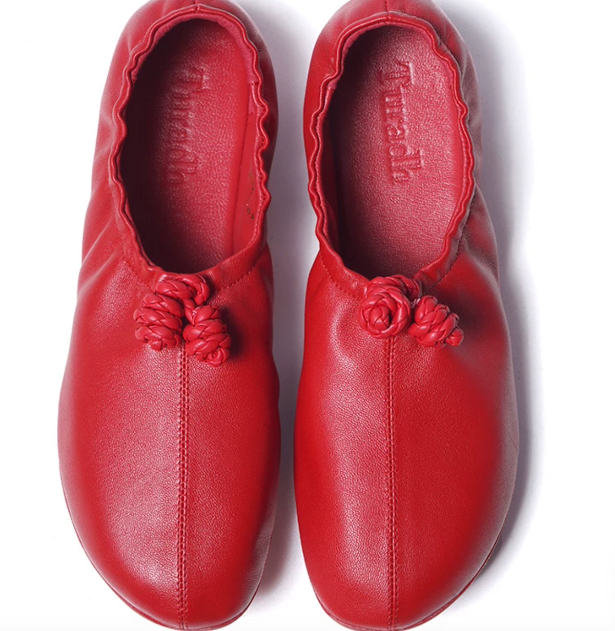 Top-down view of red sheepskin ballet flats with twin braided knots and center-front seam