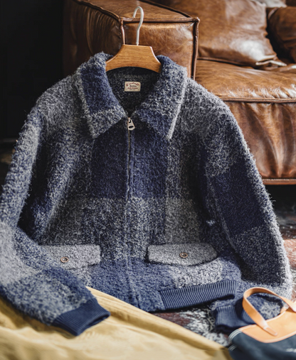 Blue-gray boucle plaid jacket hanging on wooden hanger beside leather sofa.