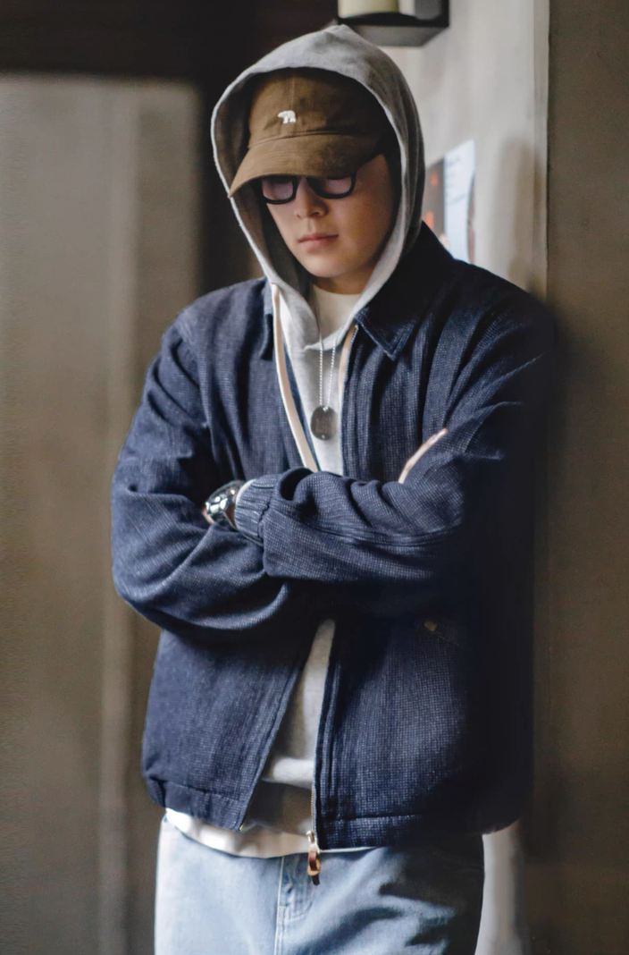 Model styling denim coach jacket layered over hoodie with cap