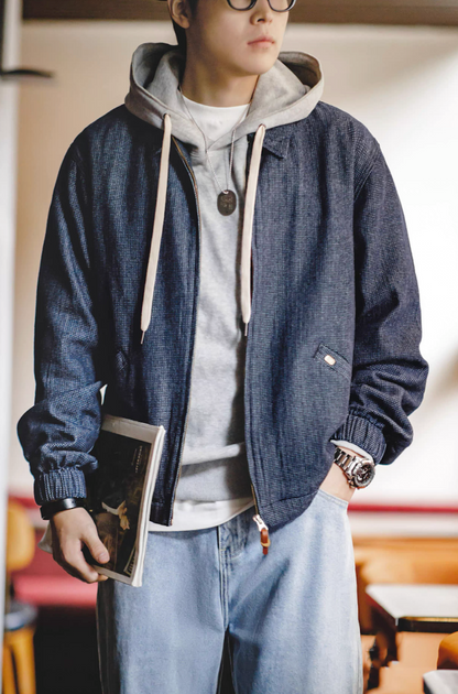 Model wearing denim coach jacket layered with hoodie holding magazine