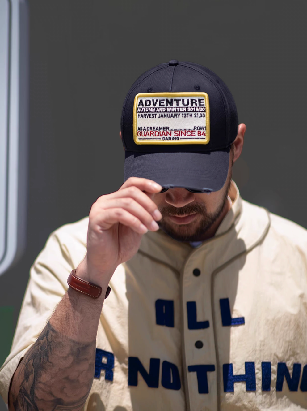 Man wearing Retro Explorer Cap dark blue adjusting brim showcasing embroidered adventure patch structured fit and casual streetwear styling