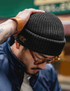 Retro Knit Beanie in Black top down view with hand adjusting fit highlighting ribbed knit texture and snug winter style