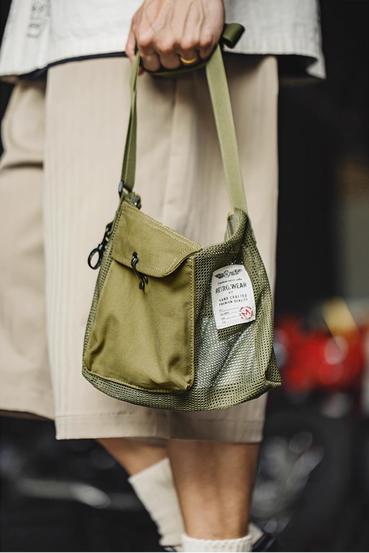 Hand carry view of green tactical mesh sling bag showing compact design