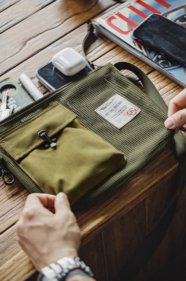 Mesh tactical sling bag on wooden desk with AirPods, keys, and magazines